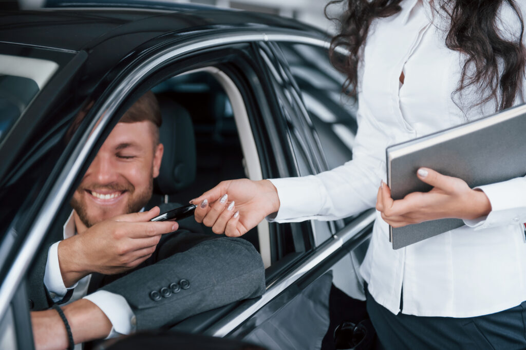 Smiling passenger in a car taking keys from a woman with a clipboard